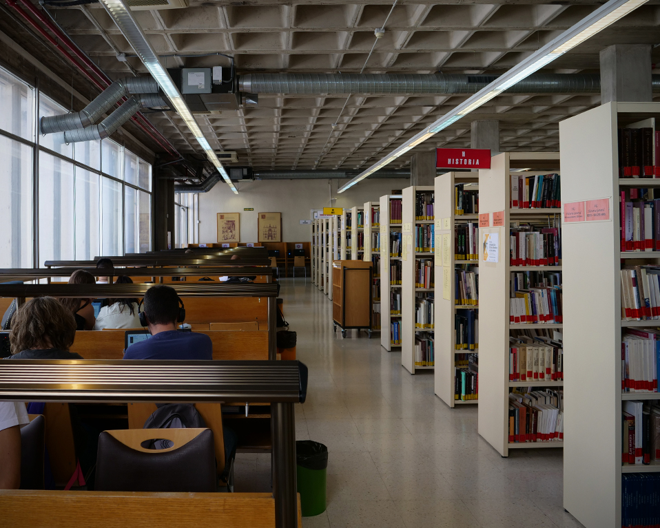 Biblioteca de la Facultad de Filosofía y Letras con varios estudiantes y estanterías con libros a la derecha