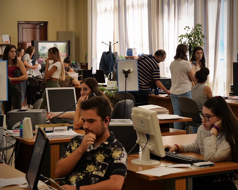 Multitud de estudiantes en una sala con ordenadores en la Facultad de Filosofía y Letras. Algunos estan charlando y otros usando los ordenadores