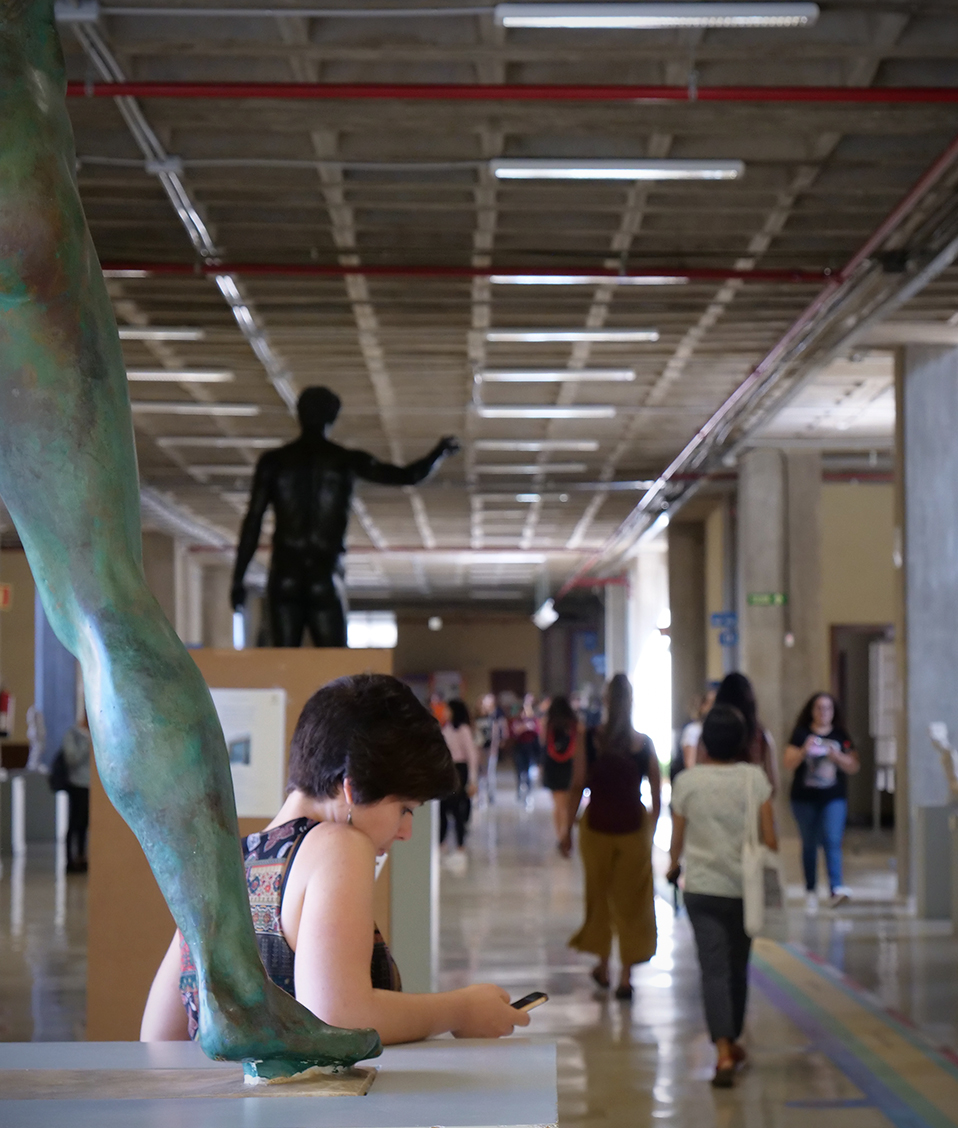 Personas transitando por algún pasillo de la Facultad de Filosofía y Letras con una estatua en el fondo